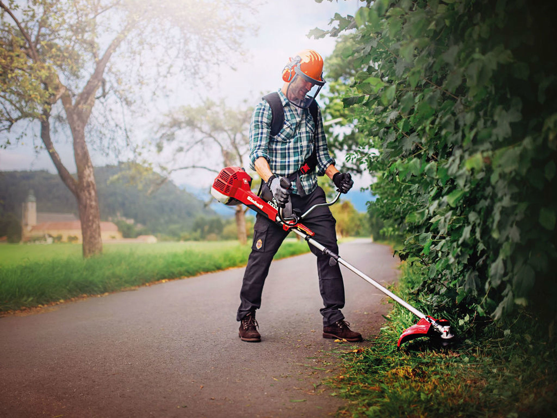 A man mows the grass under a hedge