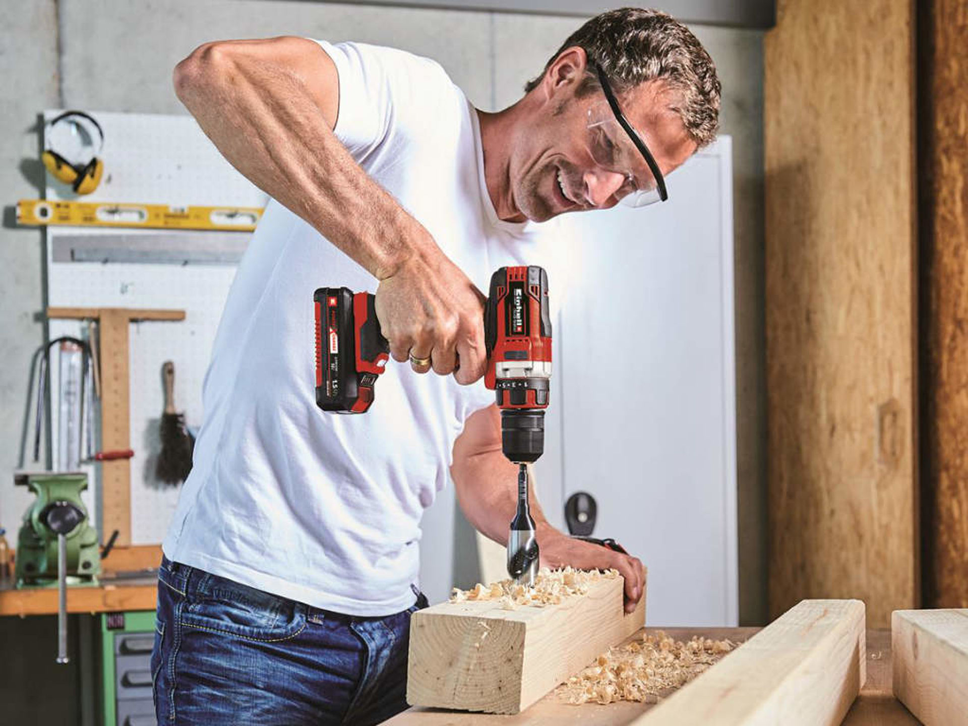 A man drills a hole in wood with a cordless drill.