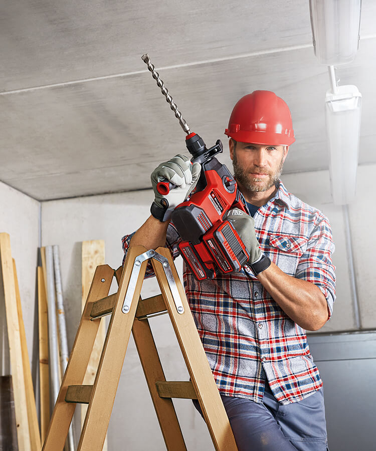 man stands on the ladder with a large drill in his hand